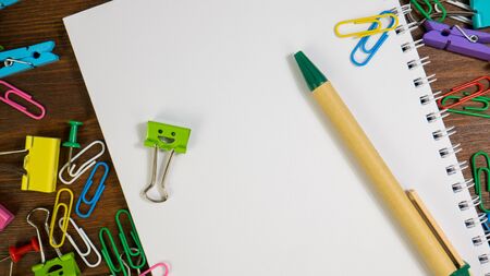 Smiles Binder Clips with School Office Supplies. Paper notebook with green pen. School stationery on brown wooden table. Concept of back to school, education or knowledgeの写真素材