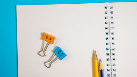 Paper Notepad with Pencils and Binder Clip on Blue Background. Spiral notebook on table. Office supplies or education conceptの写真素材