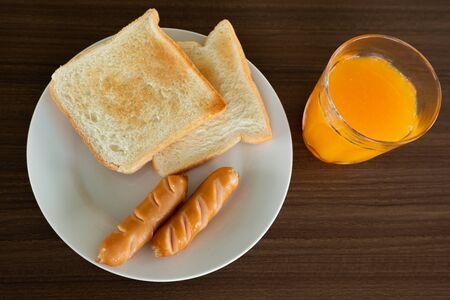 Breakfast on the table, consisting of toast, grilled sausage, fried egg and squeezed orange juiceの写真素材