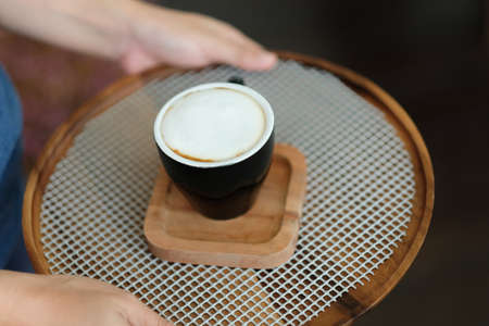 Professional waiter is serving cup of coffee on wooden trayの写真素材