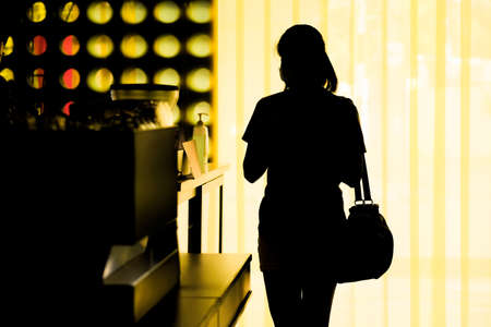 A silhouette of a woman wearing a mask while shopping for coffee in a coffee shop, spaced social distance from others during the coronavirus outbreak.の写真素材