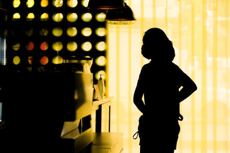 A silhouette of a woman wearing a mask while shopping for coffee in a coffee shop, spaced social distance from others during the coronavirus outbreak.の写真素材