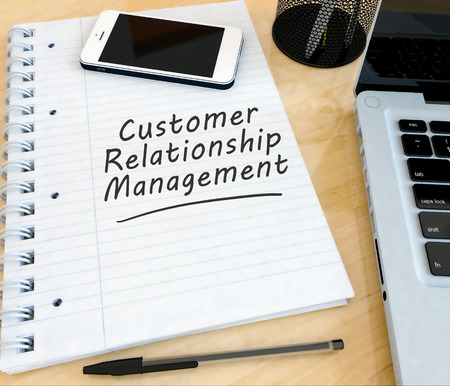Customer Relationship Management - handwritten text in a notebook on a desk with laptop and mobilephone- 3d render illustration.の写真素材