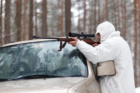 Sniper in white camouflage on jeep at winter forest.