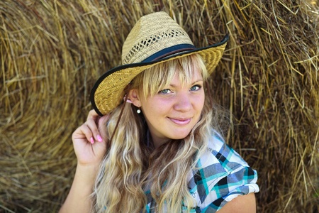 Blonde girl`s portrait in cowboy hat on straw bales background.