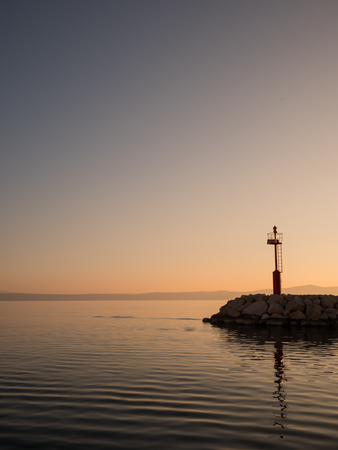 Calm sea and red lighthouse tower on port entrance at sunset in Tucepi, Croatiaの写真素材