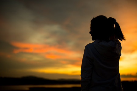 Silhouette of a young woman looking at the sunset sky.の写真素材