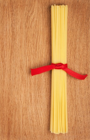 Bunch of spaghetti tied up with a red ribbon on a wooden backgroundの写真素材
