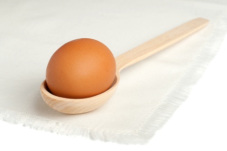 Brown egg in a wooden spoon on a white napkinの写真素材