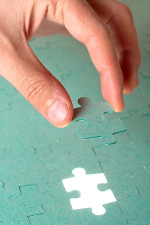 Hand inserting missing piece of green jigsaw puzzle into the holeの写真素材