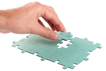Hand inserting missing piece of green jigsaw puzzle into the holeの写真素材