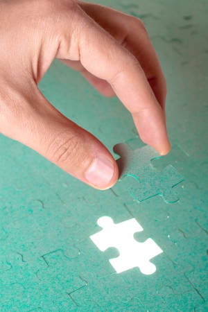 Hand inserting missing piece of green jigsaw puzzle into the holeの写真素材