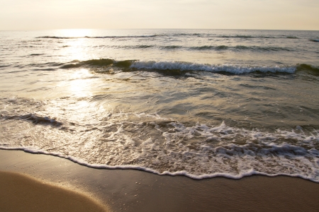 Shiny sea waves on the beach sand in sunset lightの写真素材