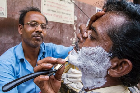 KOLKATA, INDIA - MARCH 13: Street barber shaving a man using an open razor blade on a street in Kolkata, West Bengal, India on March 13, 2013のeditorial素材