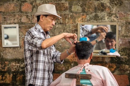 HANOI, VIETNAM - APRIL 8: Unidentified barber cut hair on street on April 8, 2014 in Hanoi, Vietnam. Barber who doesn't have a shop have to work on street.のeditorial素材