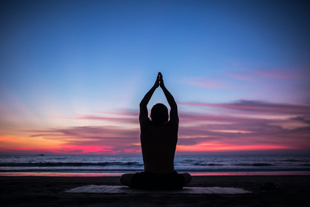 Man silhouette doing yoga exercise at sunset beachの写真素材