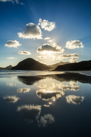 Beautiful ocean sunset. Clouds and sun light reflecting in the water on the beachの写真素材
