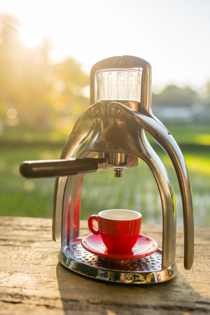 Manual old school espresso maker machine with a cup on wooden table in beautiful morning lightの写真素材