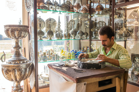 Iran, Isfahan - December 13, 2015: An old skilled artisan makes traditional metal souvenirs in a small workshop.のeditorial素材