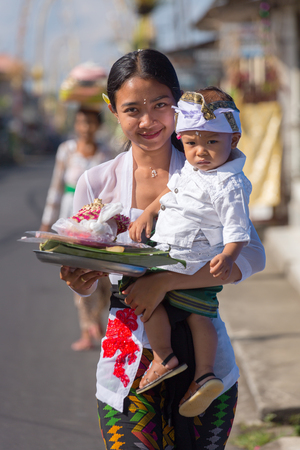 Bali, Indonesia - September 7, 2016: Unidentified balinese woman with a child carry offerings for gods during Galungan and Kuningan in Ubud, Baliのeditorial素材