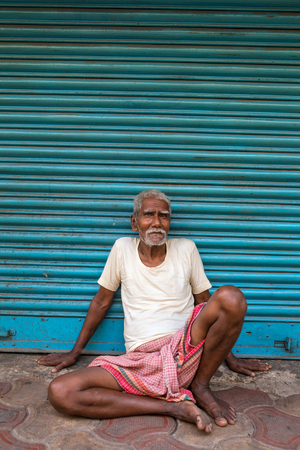 Kolkata, India - April 8, 2017: An old man sitting near the blue shutters in Kolkata, Indiaのeditorial素材
