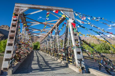 Buddhist prayer flags protect a bridge over the Inuds River in Ladakh, Indiaの写真素材
