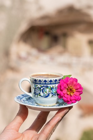 Womans hand holding a cup of traditional turkish coffee with famous Uchisar Castle at background in Cappadociaの写真素材