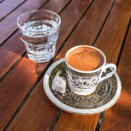 Traditional strong and dark Turkish coffee served with a glass of water on a side on a wooden table in  outdoor cafeの写真素材
