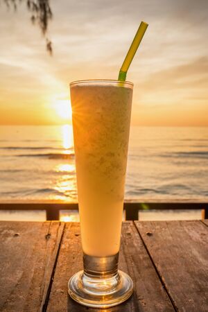 Fresh fruit juice with ice on wooden table at the tropical beach at sunsetの写真素材