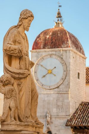 Statue of St Lawrence with Clock tower at background in Trogir, Croatiaの写真素材