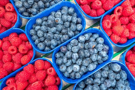 Blueberries and raspberries in blue boxes on food farmers market.の写真素材