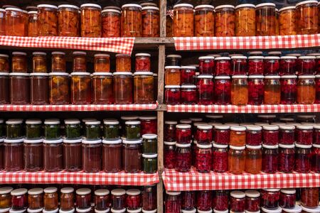 Glass jars with various types of natural delicious jam stand in a row on wooden shelves. Food backgroundの写真素材