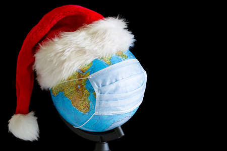 Earth globe in xmas hat and sterile medical mask at black backgroundの写真素材