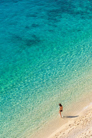 Young woman enter transparent turquoise water of the Mediterranean sea