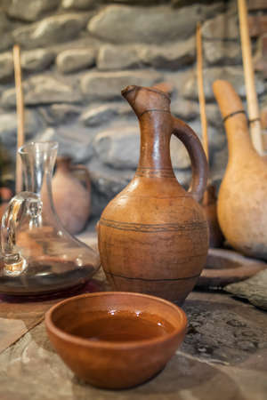 Young wine in clay bowl next to vintage georgian terracotta jug in authentic Georgian wine cellar.