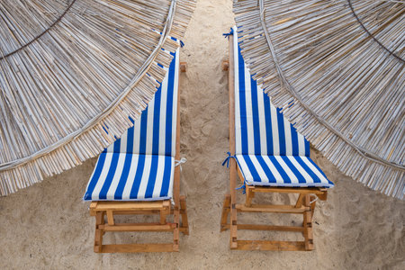 Straw beach umbrellas and two sun beds at the empty beach close-up