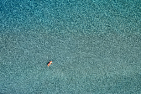 Aerial top down view of a man on the inflatable mattress on clear sea waterの写真素材