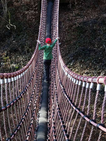 A boy walks on a swing bridgeの写真素材