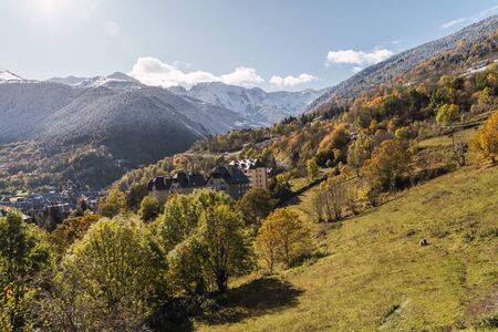 Buildings in the middle of a valley surrounded by snow-capped mountains on a sunny dayの写真素材