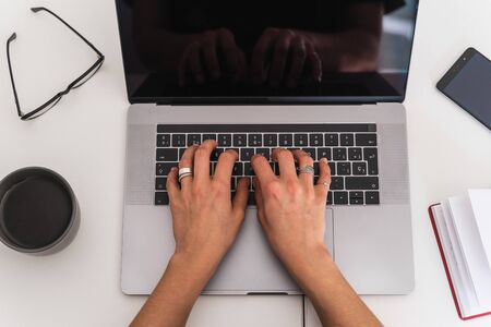 Aerial view of a woman's hands with rings using a laptop on a table with coffee, a notebook, an...