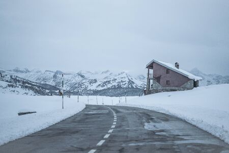 Snowy road with a snow-covered roadside building on a dark day with fog and the mountains on the...