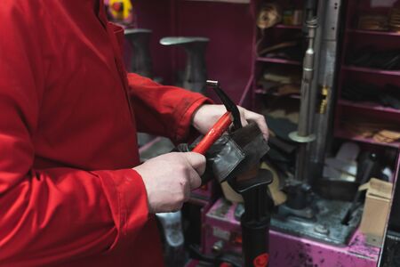 Detail of a shoemaker's hands dressed in red working with a hammer and shoes in an interior room...