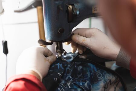 Detail of a shoemaker's hands with white gloves sewing part of a blue backpack in a textile repair shopの写真素材