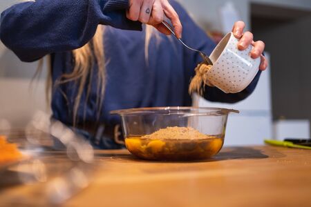Selective focus on a close-up of a woman's hands pouring sugar from a moles' cup into a glass bowl with eggs inside on a wooden tableの写真素材