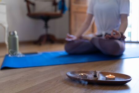 Close-up of incense and candles burning with an unfocused person behind meditating with the mobile phone and the agの写真素材