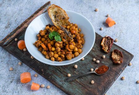 Bowl of chickpeas surrounded by its main ingredients on a wooden board on a white and light blue backgroundの写真素材