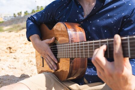 Detail of the hands of a man with a printed shirt playing the guitar in the middle of some rocksの写真素材
