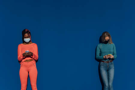 Two entertaining friends with their mobile phone keeping a safe distance and wearing a mask. Safety...