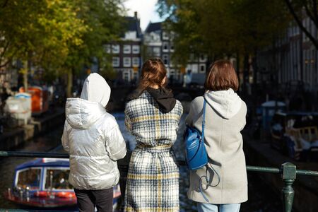 Three women standing on a bridge looking at an Amsterdam canalの写真素材