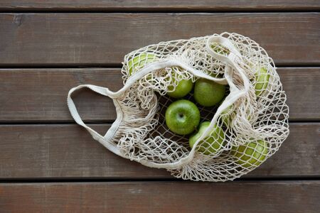 A string bag with green apples on a wooden surfaceの写真素材